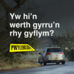 A car driving around a corner with the text "Yw hi'n werth gyrru'n rhy gyflym?"